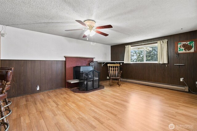 office space with a wood stove, wood finished floors, ceiling fan, baseboard heating, and a textured ceiling