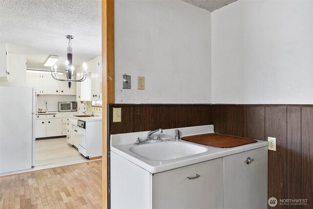 laundry room with a sink, an inviting chandelier, light wood-type flooring, and a textured ceiling