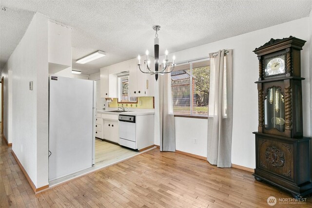 unfurnished dining area featuring baseboards, a notable chandelier, a sink, and light wood-type flooring