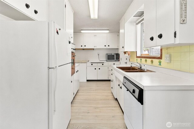 kitchen with decorative backsplash, appliances with stainless steel finishes, light wood-type flooring, a sink, and white cabinets
