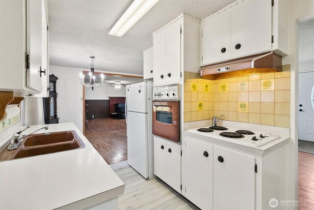 kitchen featuring a textured ceiling, light wood-type flooring, a sink, white cabinets, and white appliances