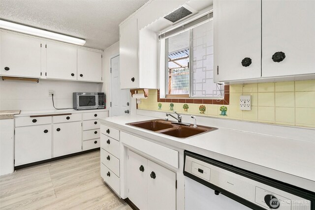 kitchen featuring white cabinets, a sink, dishwasher, stainless steel microwave, and tasteful backsplash