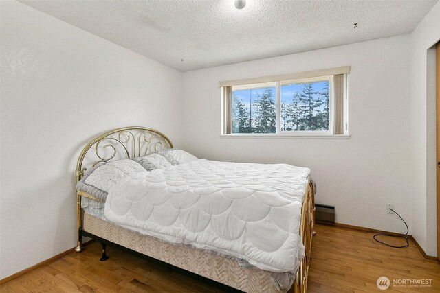 bedroom featuring light wood-type flooring, a textured ceiling, baseboards, and baseboard heating