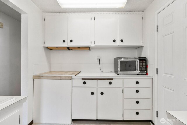 kitchen featuring light countertops, stainless steel microwave, and white cabinetry