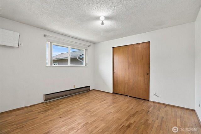 unfurnished bedroom with a textured ceiling, baseboard heating, a closet, and wood finished floors