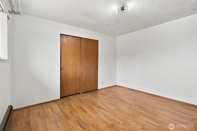 unfurnished bedroom featuring light wood-style floors, baseboard heating, a closet, and a textured ceiling
