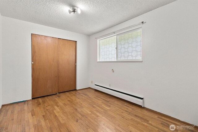 unfurnished bedroom with wood-type flooring, a textured ceiling, baseboard heating, and a closet