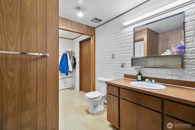 bathroom with vanity, toilet, tile patterned floors, brick wall, and visible vents
