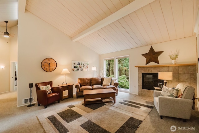 carpeted living room with ceiling fan, visible vents, a tiled fireplace, beam ceiling, and high vaulted ceiling