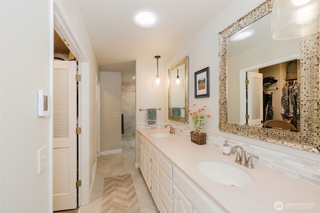 full bathroom with double vanity, a sink, walk in shower, and a spacious closet