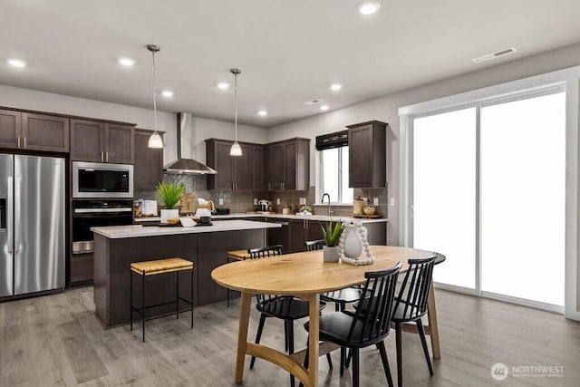 kitchen with visible vents, appliances with stainless steel finishes, dark brown cabinets, and wall chimney range hood