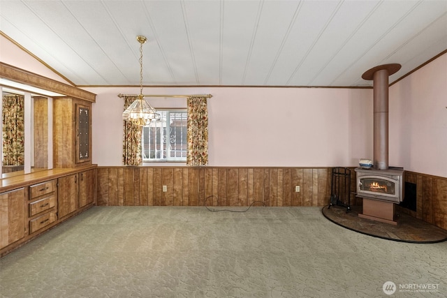 interior space featuring wood walls, a notable chandelier, a wood stove, and a wainscoted wall