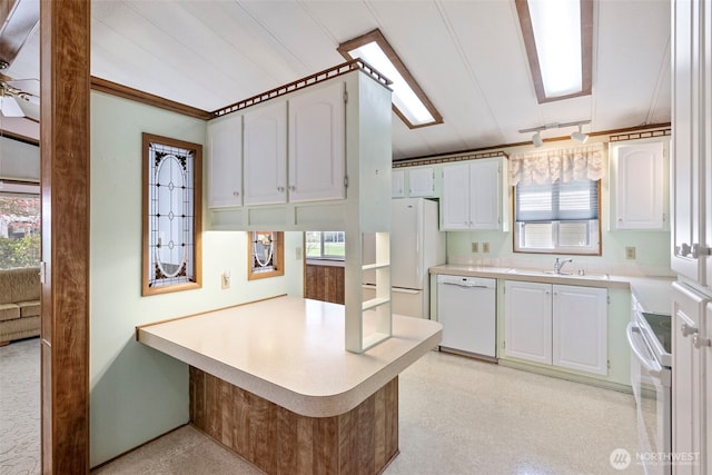 kitchen featuring light countertops, a sink, a peninsula, white appliances, and white cabinetry