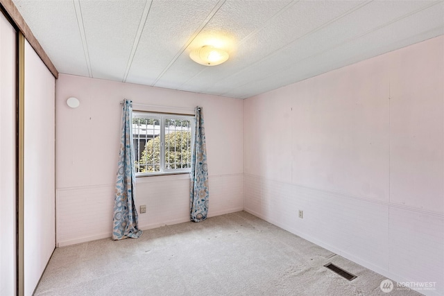 carpeted empty room featuring a textured ceiling and visible vents