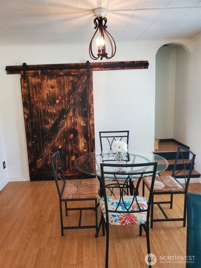 dining room featuring light wood-style floors, arched walkways, baseboards, and a barn door