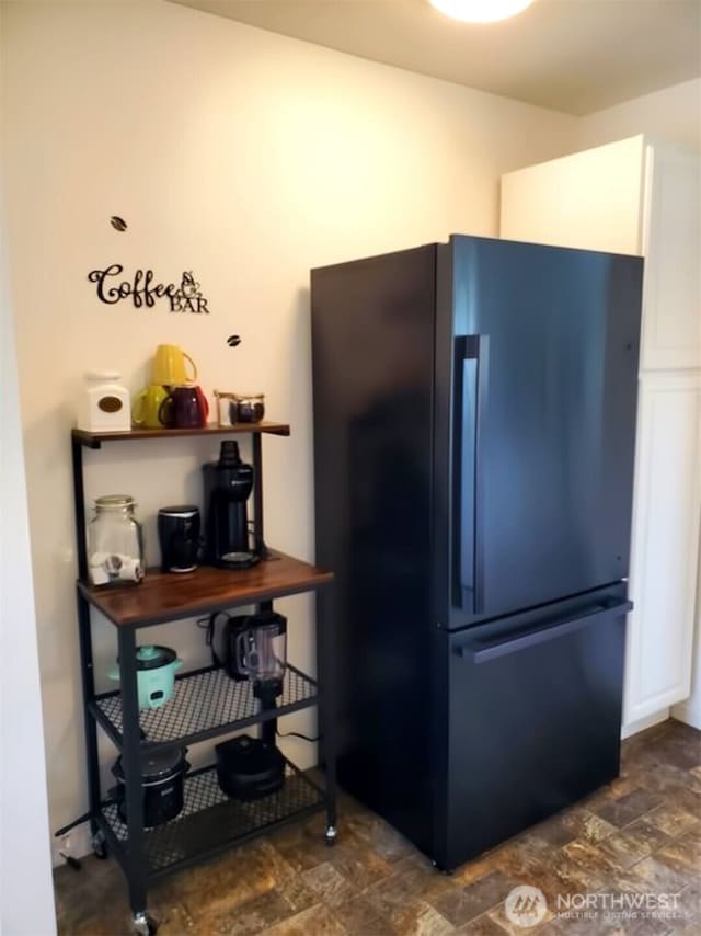 kitchen with white cabinetry, black fridge, and stone finish floor