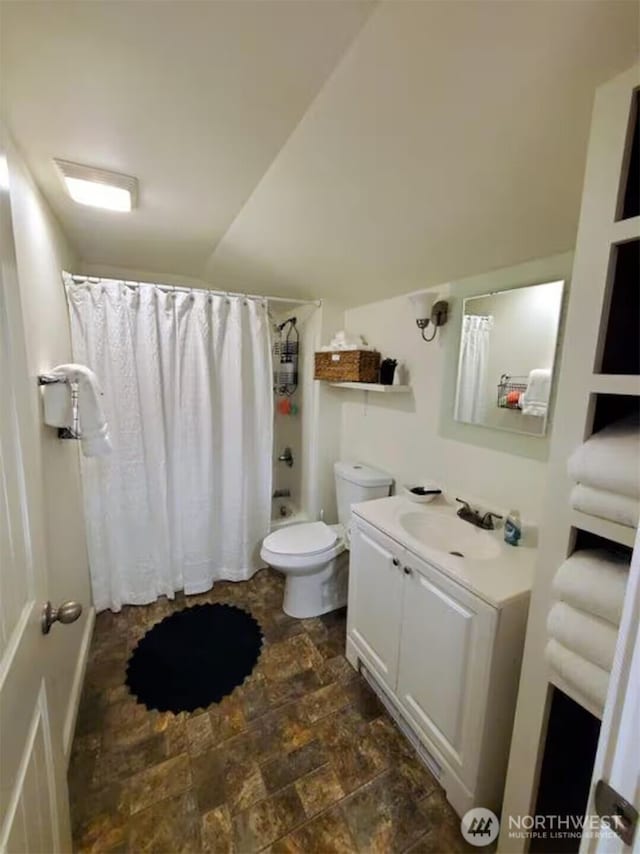 bathroom featuring toilet, shower / bath combo with shower curtain, stone finish floor, and vanity