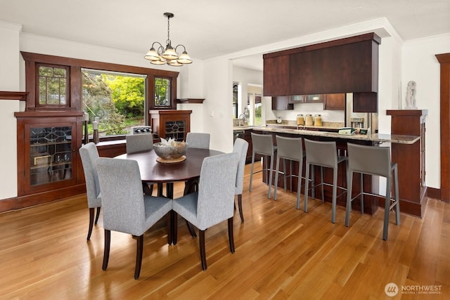 dining space with a fireplace, a chandelier, ornamental molding, and light wood-type flooring