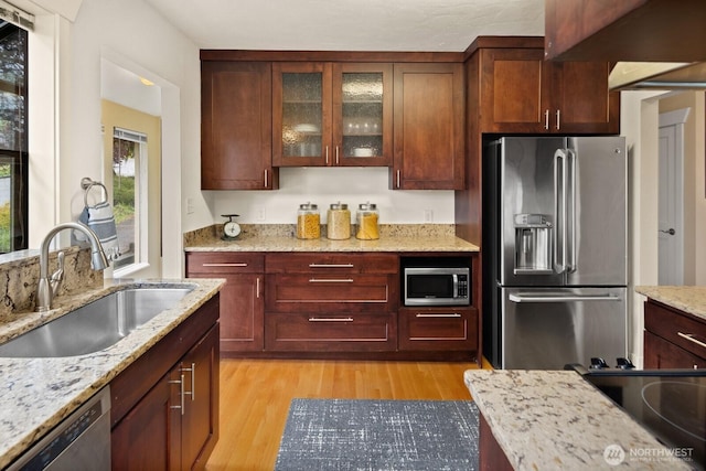 kitchen featuring light stone countertops, light wood-type flooring, a sink, glass insert cabinets, and stainless steel appliances