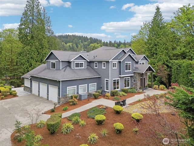 view of front of house with a view of trees, central air condition unit, driveway, and stone siding