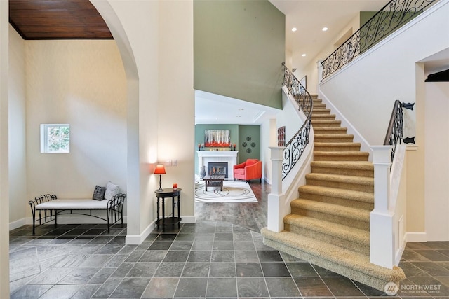 stairway with arched walkways, a fireplace, baseboards, a high ceiling, and recessed lighting