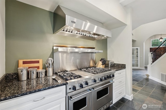 kitchen featuring white cabinets, double oven range, ventilation hood, and dark stone countertops