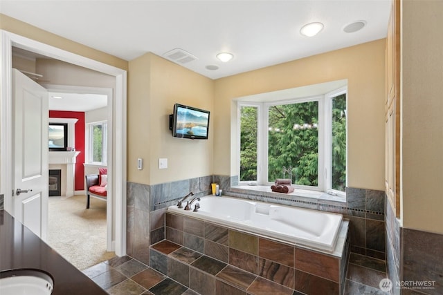 bathroom with visible vents, a glass covered fireplace, a bath, and a healthy amount of sunlight