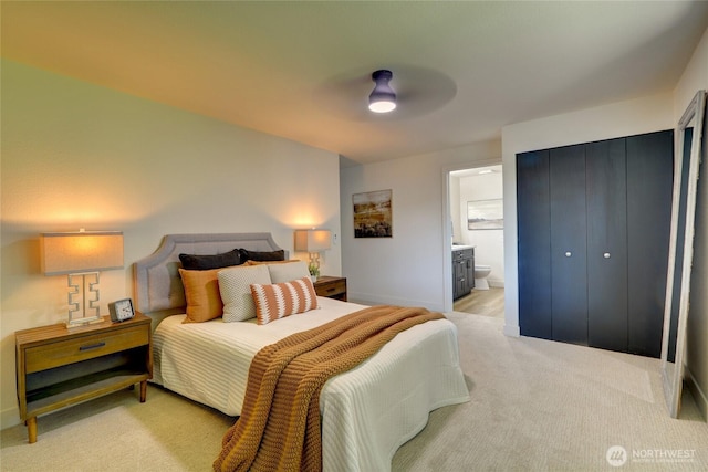bedroom featuring baseboards, ensuite bathroom, light carpet, and ceiling fan