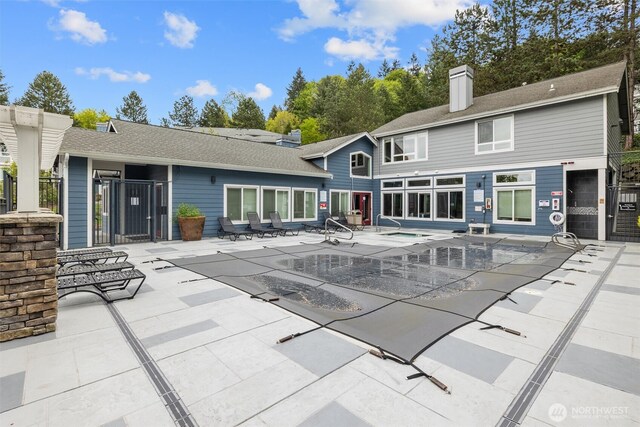 rear view of house with fence, a covered pool, an in ground hot tub, a chimney, and a patio