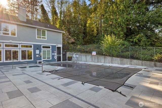 community pool with a patio, a hot tub, and fence