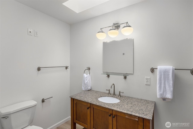 bathroom featuring vanity, baseboards, toilet, and a skylight