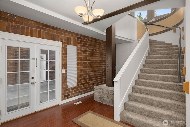 stairs with french doors, brick wall, visible vents, wood finished floors, and a chandelier