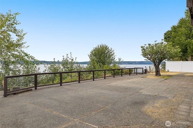 view of car parking featuring a water view and fence