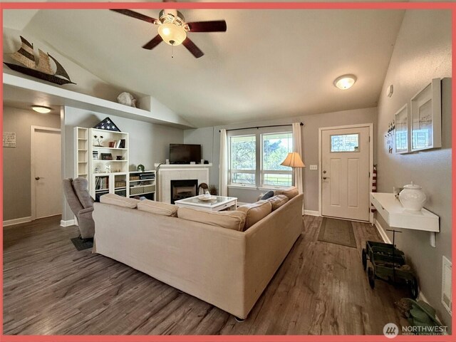 living room featuring vaulted ceiling, dark wood-style flooring, a fireplace, a ceiling fan, and baseboards