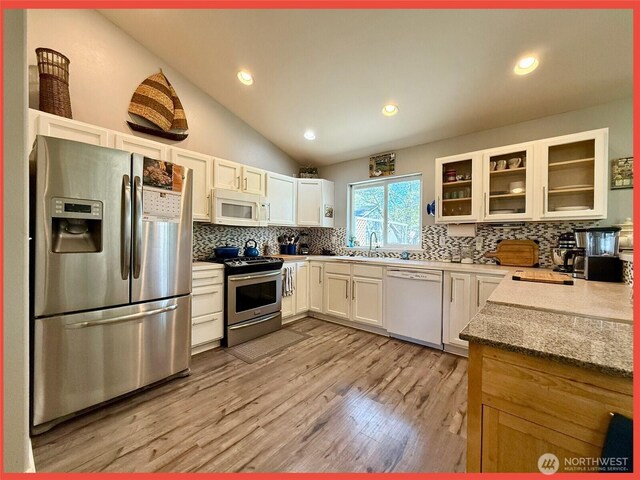 kitchen with appliances with stainless steel finishes, backsplash, glass insert cabinets, light wood finished floors, and white cabinetry