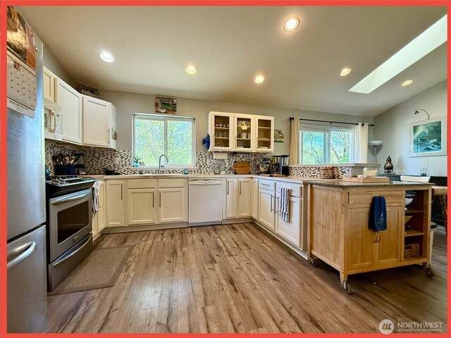 kitchen featuring stainless steel appliances, a sink, a peninsula, a skylight, and wood finished floors