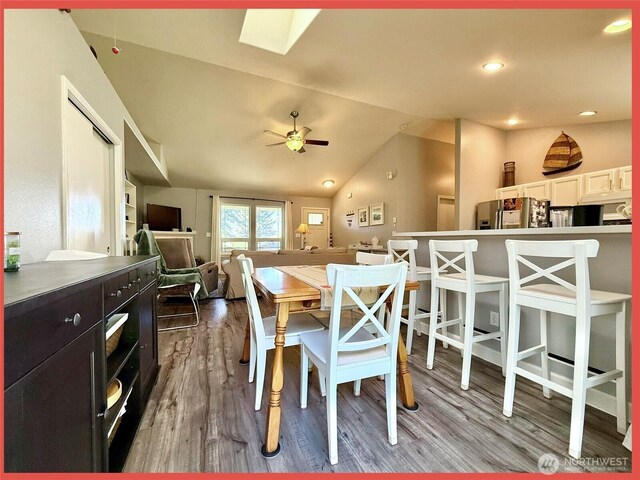dining space featuring wood finished floors, lofted ceiling, ceiling fan, and a skylight