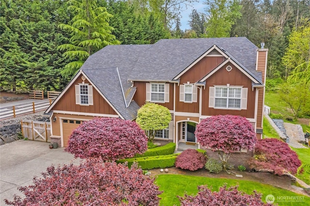 view of front of home with board and batten siding, a chimney, roof with shingles, fence, and concrete driveway