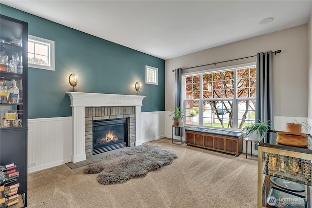 living area with carpet floors, a brick fireplace, and a wainscoted wall