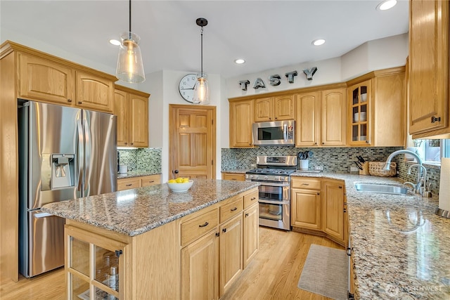 kitchen featuring a kitchen island, light stone countertops, a sink, glass insert cabinets, and stainless steel appliances
