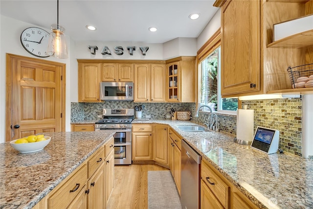 kitchen with glass insert cabinets, light stone counters, a sink, light wood finished floors, and stainless steel appliances