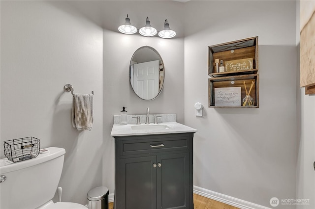half bath featuring vanity, baseboards, wood finished floors, and toilet