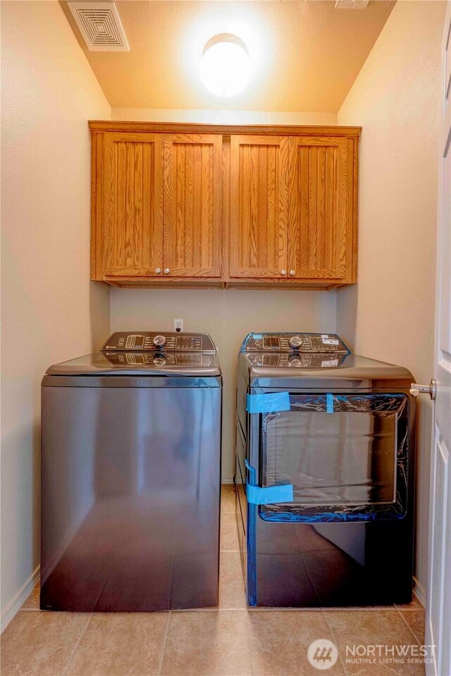 clothes washing area with independent washer and dryer, cabinet space, light tile patterned floors, and baseboards