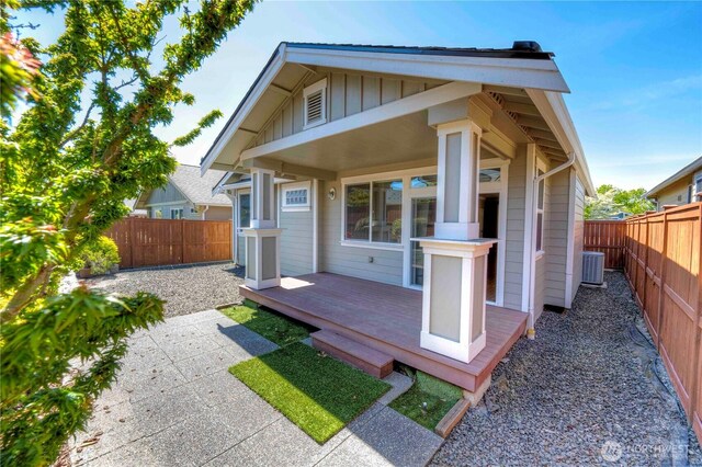 rear view of property with board and batten siding, a fenced backyard, central AC, and a wooden deck