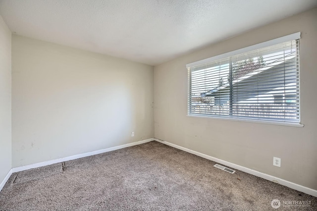 spare room featuring carpet floors, baseboards, a textured ceiling, and visible vents