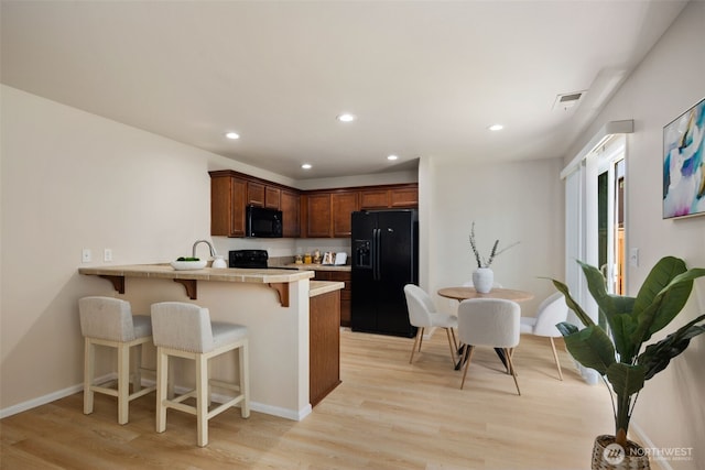 kitchen with a kitchen bar, visible vents, light wood-type flooring, black appliances, and a peninsula