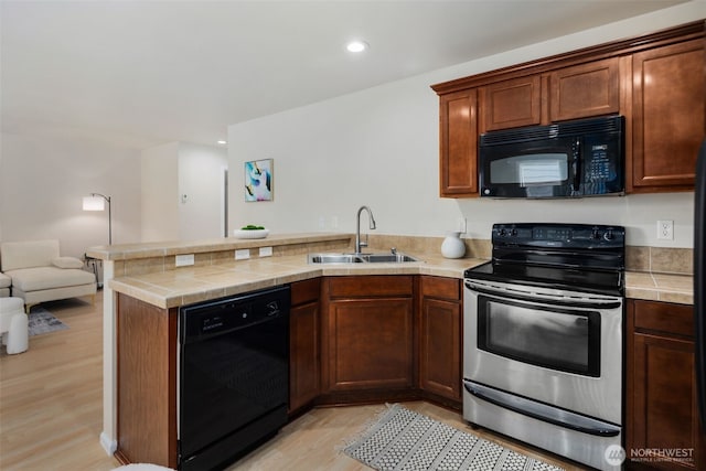 kitchen featuring a sink, light wood-style floors, a peninsula, open floor plan, and black appliances
