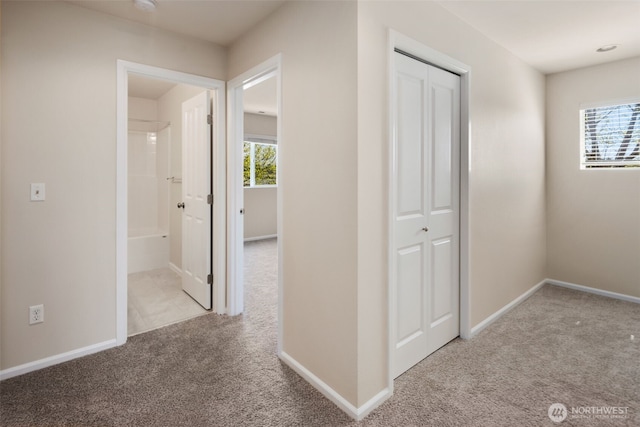 hall featuring baseboards, carpet flooring, and a healthy amount of sunlight