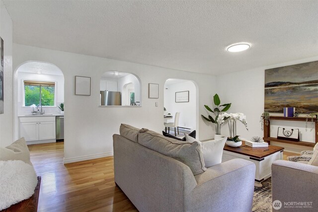 living area featuring light wood-style floors, arched walkways, baseboards, and a textured ceiling