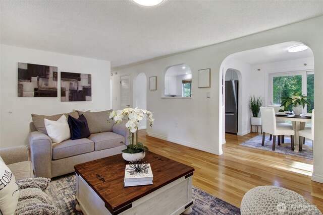 living room featuring arched walkways, baseboards, and light wood-type flooring